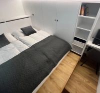 Bedroom in a studio apartment with a double bed and storage space, floor with wooden decor.