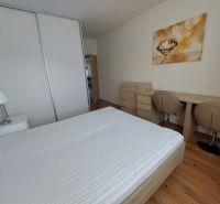 A bedroom with wood-patterned flooring, a bed, a desk, and wardrobes in a three-room apartment.