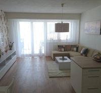 Living room in a three-room apartment with a wooden-patterned floor and floral wallpaper.