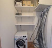 Utility room in a 3-room apartment with a washing machine and shelves, floor with wooden decor.