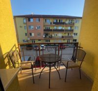 The balcony of a 2-room apartment in Vlčkovce with a table and chairs, view of the apartment building.