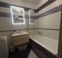 A bathroom with a mirror and a bathtub in a 2-room apartment; white tiles combined with mosaic.