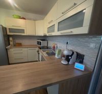 A kitchen in a 2-room apartment with a wooden decor floor and light furniture.