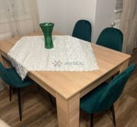 Dining table with a vase and green chairs, wooden decor flooring in a 2-room apartment.