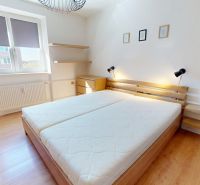 Bright bedroom in a 2-room apartment with wood-patterned flooring and a double bed.