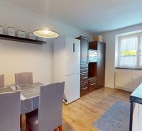 A kitchen in a 2-room apartment with light walls and appliances, and a floor with a wood decor.