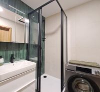 A bathroom of a 2-room apartment with a modern shower, a washing machine, and green tiles.