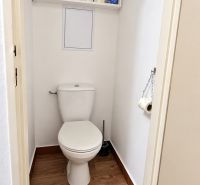 A toilet with a shelf and a wooden decor floor in a 3-room apartment.