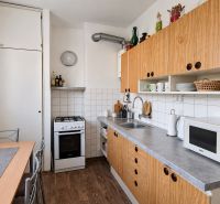 A kitchen in a 3-room apartment with a kitchen unit, appliances, and flooring with a wooden decor.