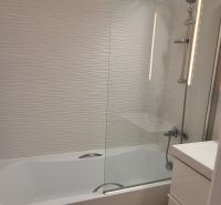 A bathroom in a 3-room apartment with a bathtub, white tiles, and a floor with a wooden decor.