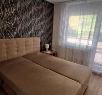 Bedroom with upholstered bed, patterned wallpaper, curtains, wooden decor flooring.