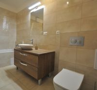 Bathroom with a bathtub, a sink on a wooden decor, and beige tiles in a 3-room apartment.