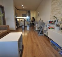 Living room in a three-room apartment with a wooden decor floor, a sofa set, and a kitchen.