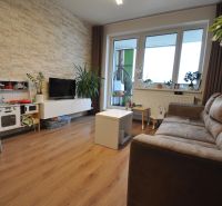 A living room in a three-room apartment with a wooden decor floor and stone cladding on the wall.