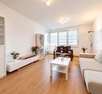 Living room in a two-room apartment with a wooden decor floor and light furniture.
