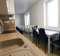 A kitchen in a 2-room apartment with white furniture, blue chairs, and a wooden-patterned floor.