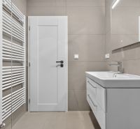 A bathroom in a 3-room apartment with a shower, light tiles, and white furniture.