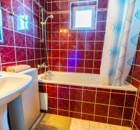 A bathroom in a family house with red tiles, a bathtub, and a sink.