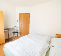 Bright bedroom with a bed, wardrobe, and wood-patterned floor in a family house.
