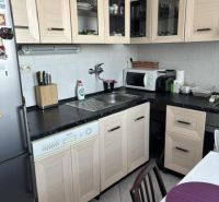 A kitchen in a two-room apartment with wooden decor furniture and light tiles.