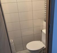 A toilet with simple tiles and flooring in a 2-room apartment.
