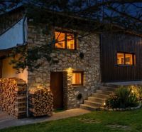 A night view of a stone family house in Dobrá Voda with a wood storage and garden lighting.