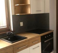 A kitchen unit in a 2-room apartment with a black sink and white cabinets.