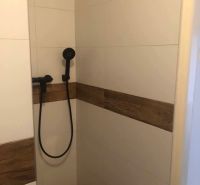Shower corner with ceramic tiles and a showerhead in a 2-room apartment.
