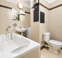 Bathroom in a studio apartment with a bathtub, sink, and toilet, tiled with light tiles.