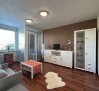 Living room in a two-room apartment with a wooden decor floor, white furniture, and light-colored walls.