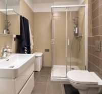 A bathroom in a 2-room apartment with a modern shower, built-in sink, and light tiles.