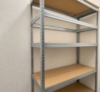 A metal shelf unit with shelves in a 2-room apartment on a white wall and grey floor.