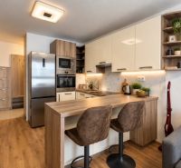 A kitchen in a 2-room apartment with appliances and a wooden decor floor.