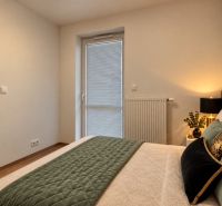 A bedroom in a two-room apartment with a green bedspread and a wooden decor floor.