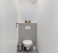 A narrow toilet with white walls and gray tiles in a two-room apartment.