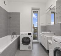 Bathroom with a bathtub, washing machines, and a sink in a 2-room apartment. Gray tiles, large mirror.