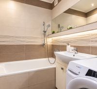 Bathroom with a bathtub and a sink in a 3-room apartment with a mirror and a washing machine.