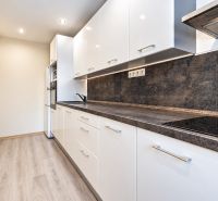 A kitchen in a 3-room apartment with white furniture and a wooden decor floor.