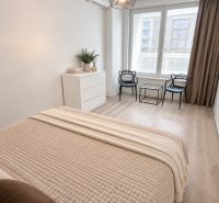 A bright bedroom in a two-room apartment with a wood-patterned floor and simple furniture.