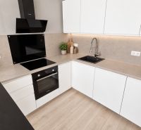 A kitchen in a 2-room apartment with white cabinets, a cooktop, and a wooden decor floor.