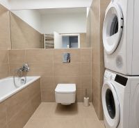 Bathroom of a 2-room apartment with a shower, washing machine, dryer, and beige tiles.