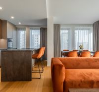 Interior with wood-patterned flooring, orange sofa, and dining table. Apartment construction.