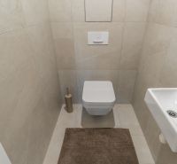 Toilet with a wall-hung toilet, small sink, and beige tiles, Apartment construction.