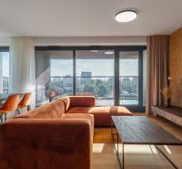 Living room with an orange sofa, dining table, and a view of the city. Apartment construction.