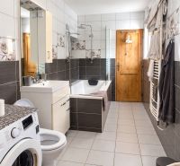 A bathroom in a family house with a washing machine, a bathtub, and tiles in neutral colors.