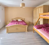 A bedroom in a family house with a large bed, a bunk bed, and a floor with a wooden decor.