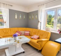 Corner sofa in the living room of a family house with floral decoration and wooden decor flooring.