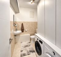 A bathroom in a family house with a washing machine, dryer, and beige tiles.