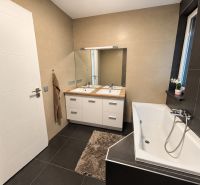 Bathroom in a family house with a bathtub, mirror, and cabinet under wooden decor.