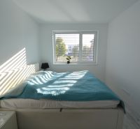 A bright bedroom with a large window, a bed, and nightstands in a three-room apartment.